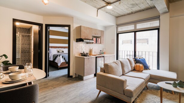A modern living room with a sofa, a dining table with bowls and glasses, a kitchen with a dishwasher, and a large window with a view. - Vivo One Zona 1 Guatemala (Guatemala City)