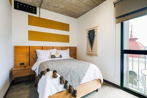 Una cama bien hecha con una manta gris y blanca, un cabecero de madera y una mesita de noche de madera a su lado.