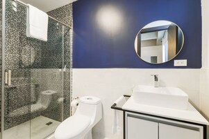 A modern bathroom with a glass-enclosed shower, a white toilet, a sink with a mirror above it, and a blue accent wall.
