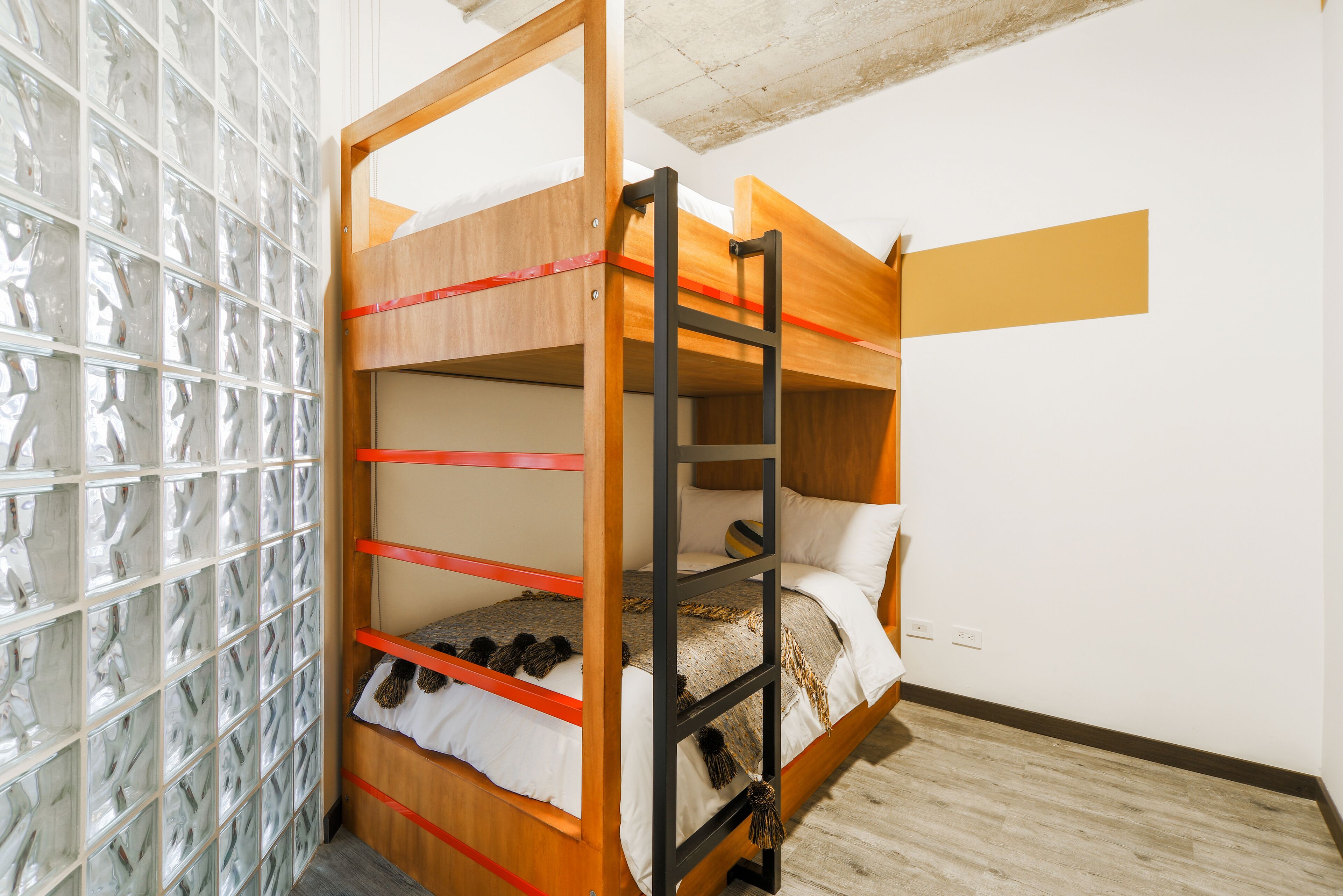 Een stapelbed met een ladder, een muur van glasblokken en een houten vloer.