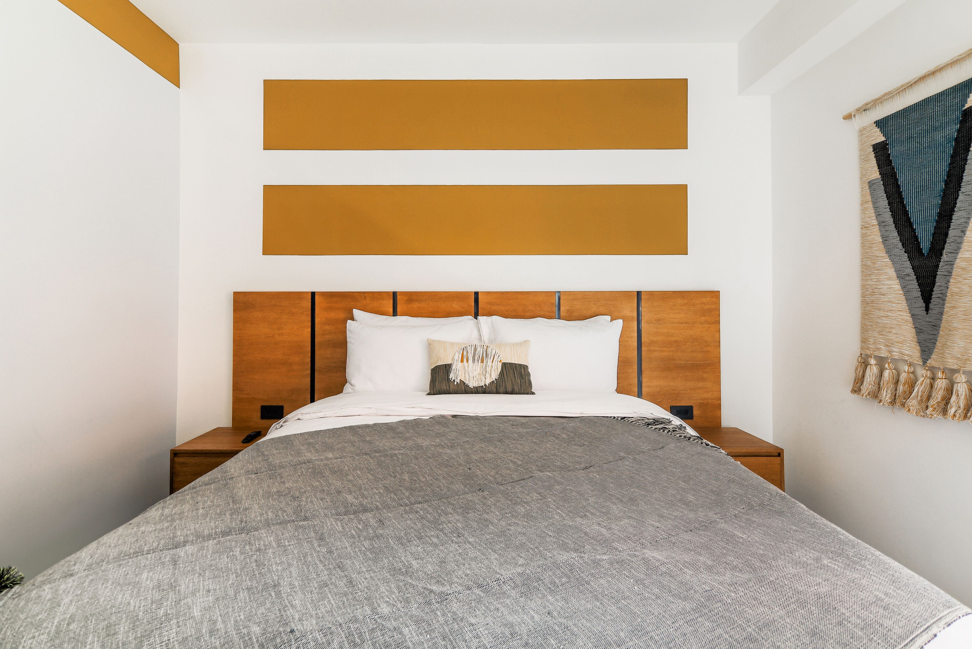 A neatly made bed with a gray blanket, wooden headboard, and a hanging light fixture.