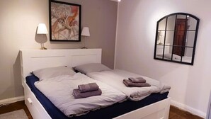 A bedroom with a bed, two bedside tables, a wall-mounted mirror, and a painting.