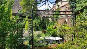 A rustic garden with a metal pergola, a round table, and potted plants. - Ehemalige Bibliothek: Küche Kamin Netflix Hofladen (Steinhöfel)