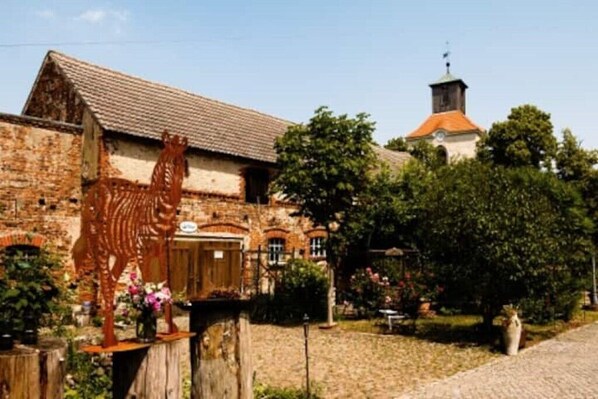 A rustic building with a brick facade, a wooden sculpture, and a church in the background.