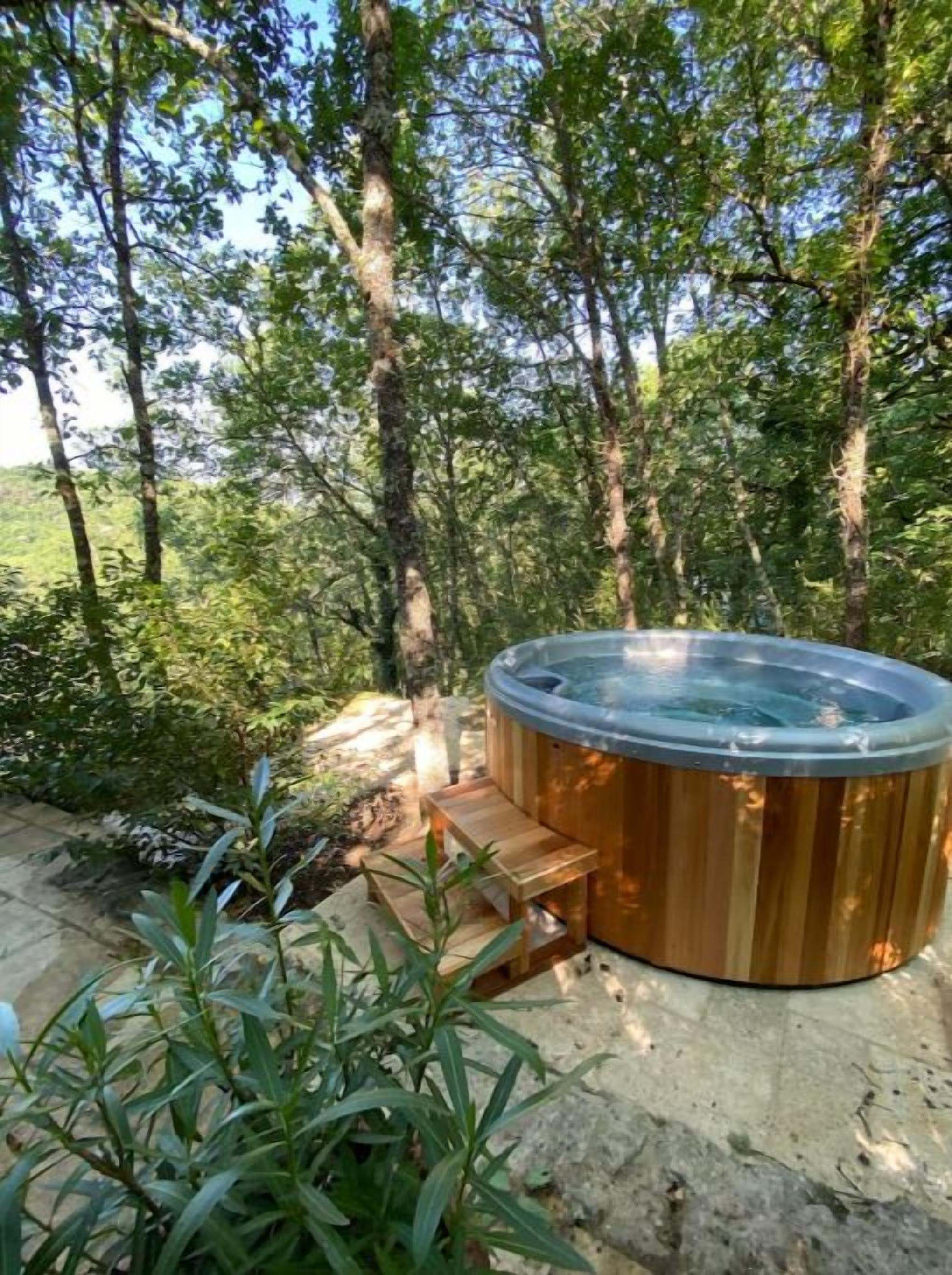 Un jacuzzi en un área boscosa con un banco de madera y un sendero de piedra.