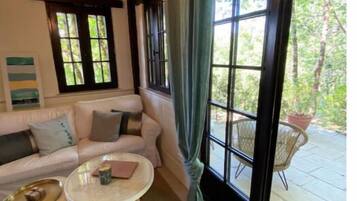 Ein gemütliches Zimmer mit Holzbalkendecke, einer Couch, einem runden Couchtisch und Blick ins Freie durch große Fenster.
