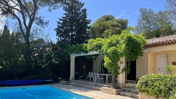 Une piscine avec une terrasse carrelée, une pergola dotée d’un espace salon extérieur et une végétation luxuriante.