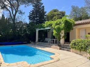 A swimming pool with a tiled deck, a pergola with outdoor seating, and lush greenery. - Cosy villa with swimming pool in a quiet area walking distance to the beach (Saint-Raphaël)