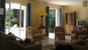 Un salon avec des meubles en osier, un téléviseur et une vue sur une piscine.