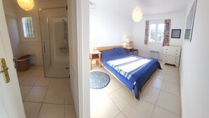 Une chambre à coucher comprenant un lit, une table de chevet, une lampe, une commode et une fenêtre avec des rideaux.