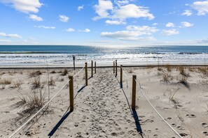 A sandy beach path leading to the ocean with wooden posts and ropes.