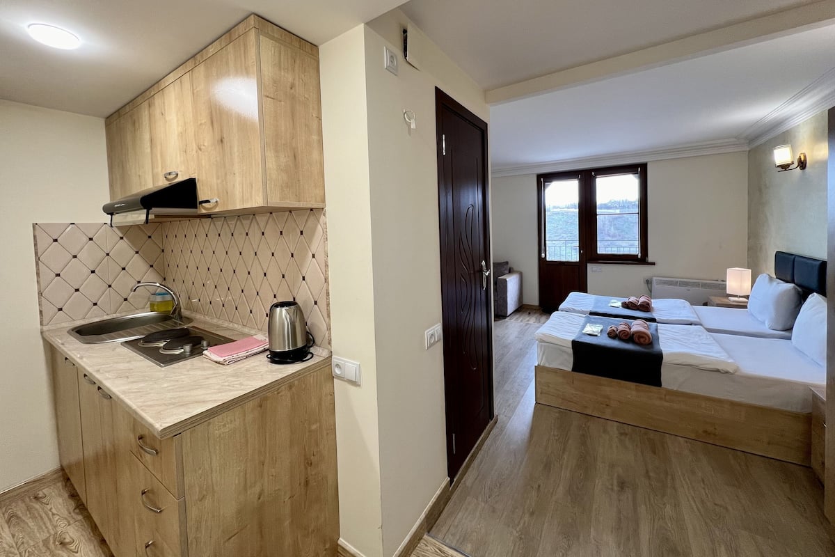 A compact hotel room with a kitchenette, a bed with two pillows, a small table with towels, and a view of the sea through the window.