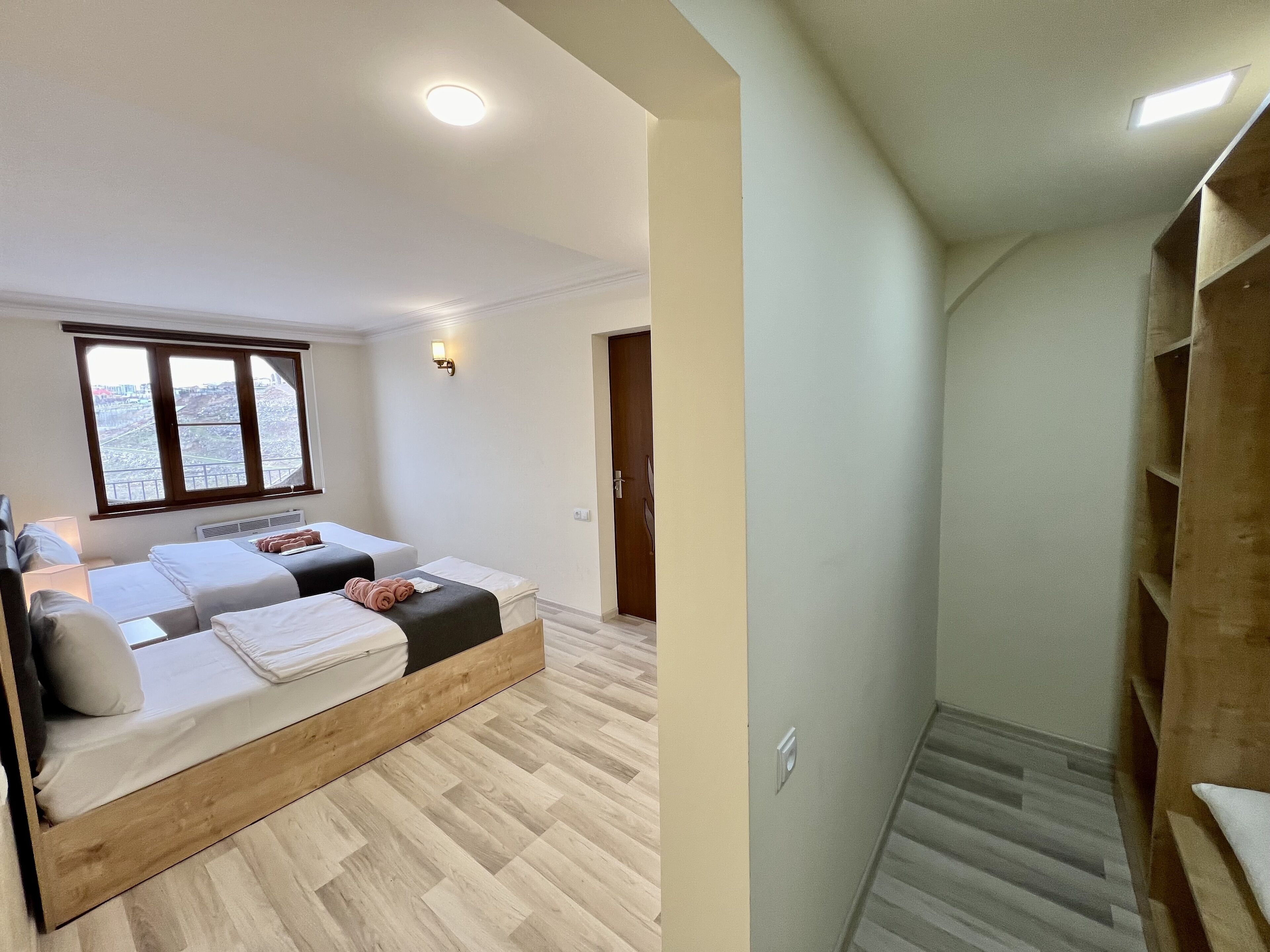 Una camera d'albergo moderna con due letti, un'ampia finestra e una scala in legno.