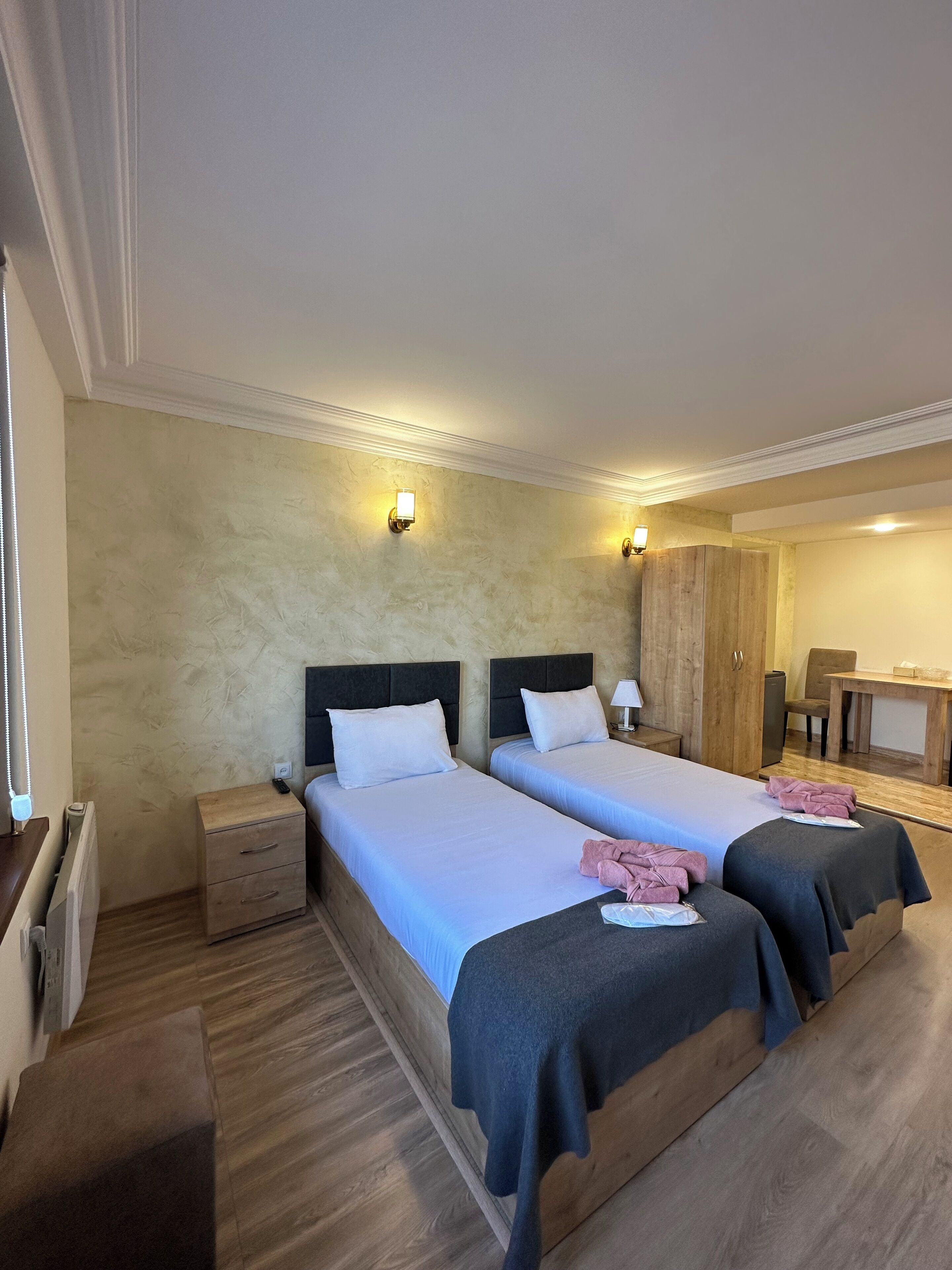Een hotelkamer met twee bedden, nachtkastjes, een houten garderobe, een bureau en een stoel.