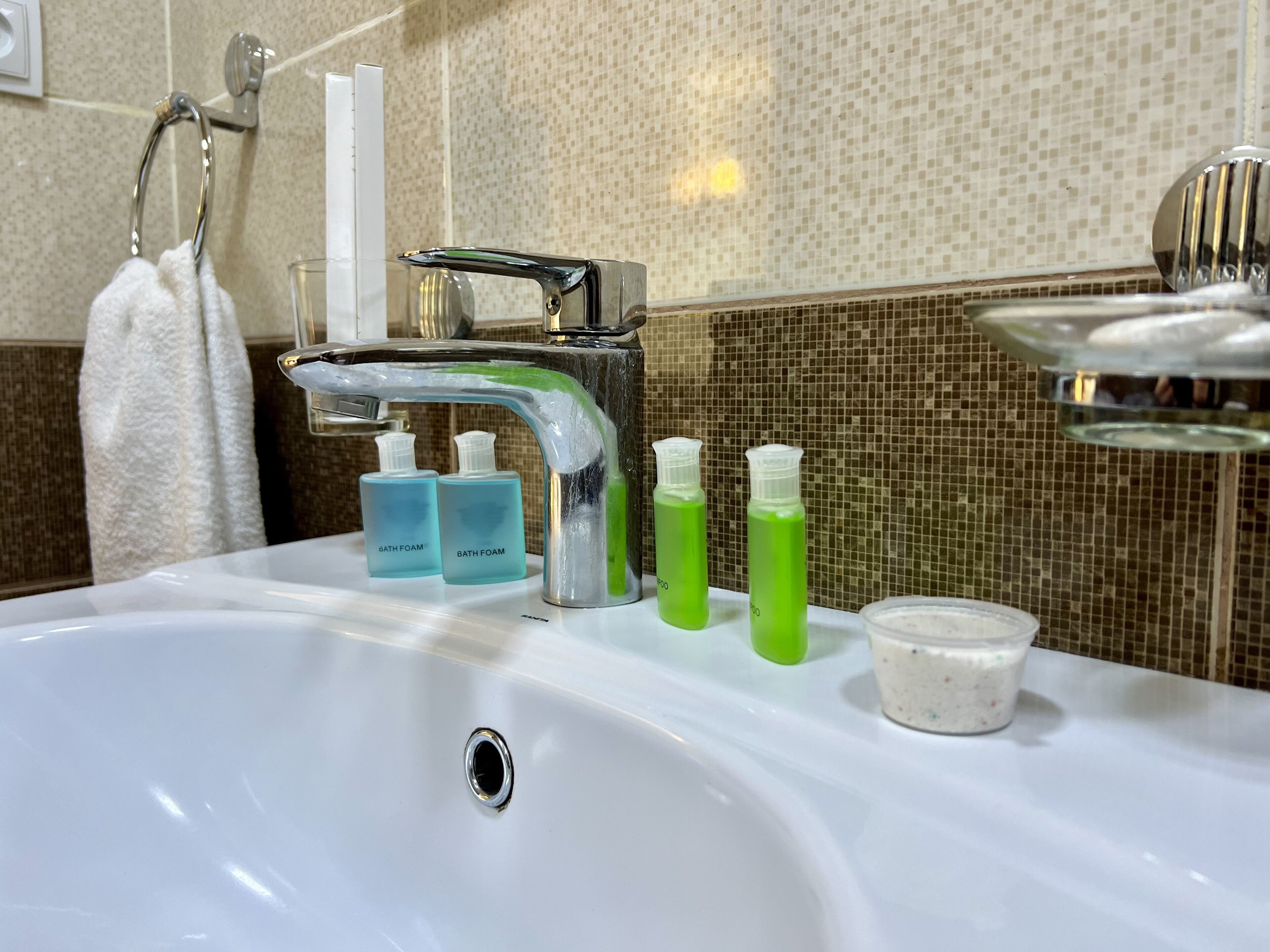 A bathroom sink with a chrome faucet, two bottles of bath foam, and a container of soap.