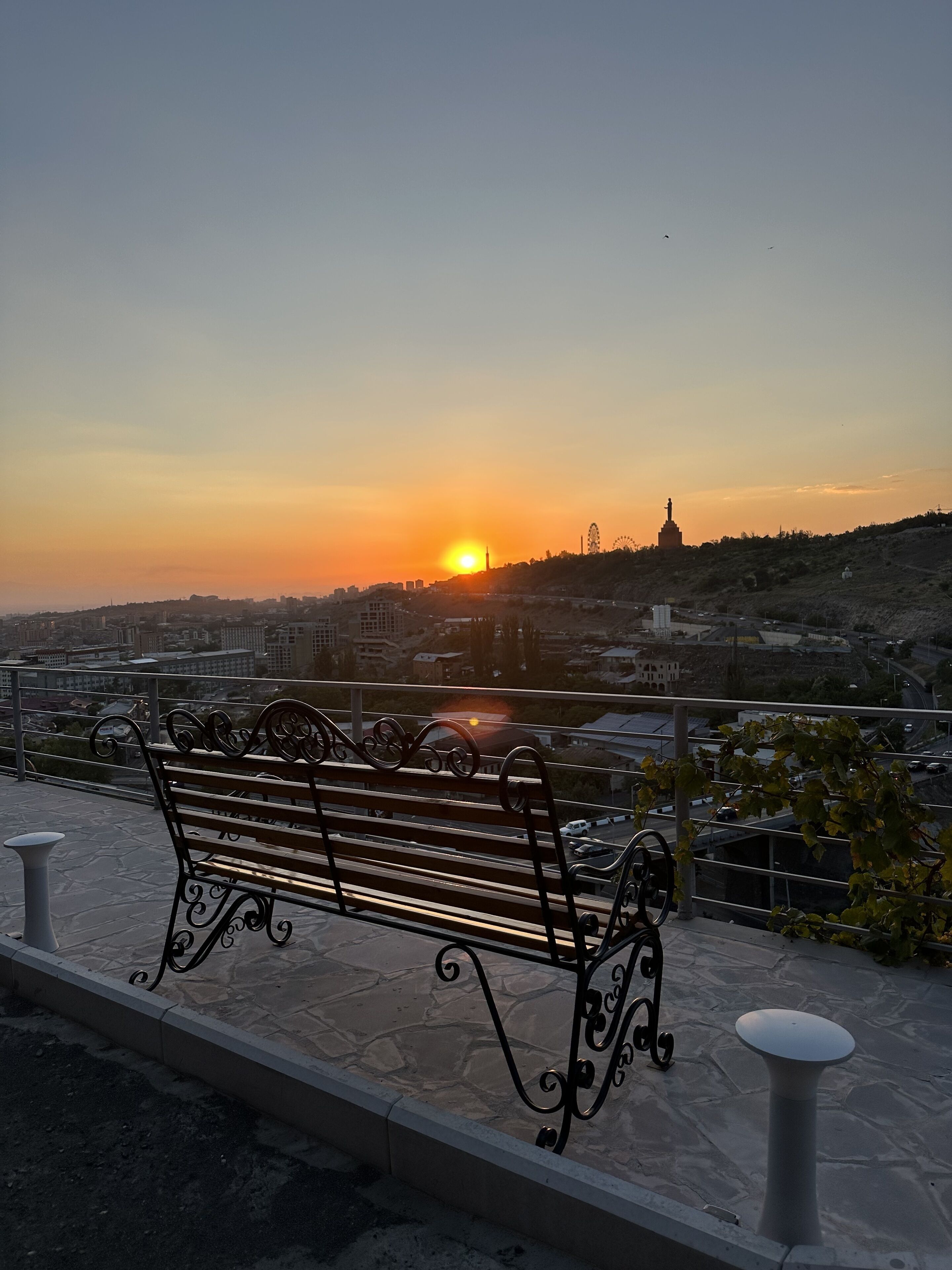 A bench overlooking a cityscape with a sunset.