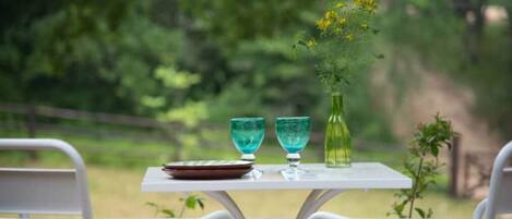A table with two turquoise glasses and a green bottle, set against a stone wall with a view of a forested area.