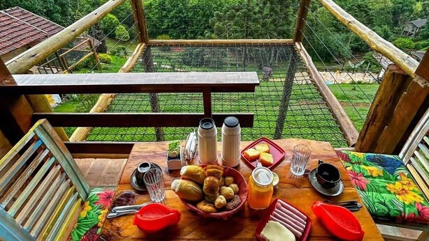 A wooden table set with food and drinks, overlooking a lush green landscape. - Canto dos Pássaros (Santo Antonio do Pinhal)