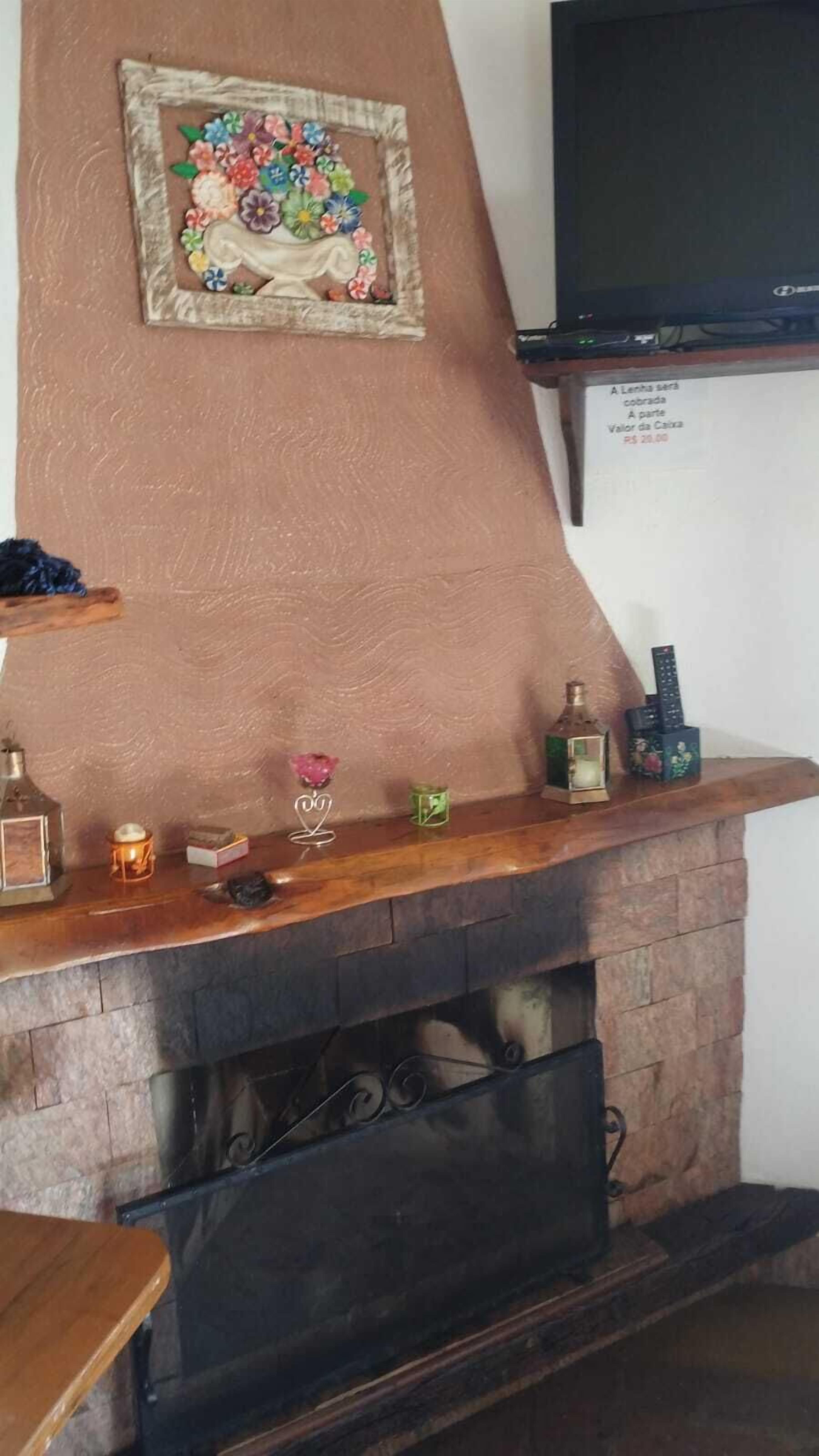 A fireplace with a mantel decorated with various items, a television mounted on the wall, and a sign indicating a price of R$ 20.00.