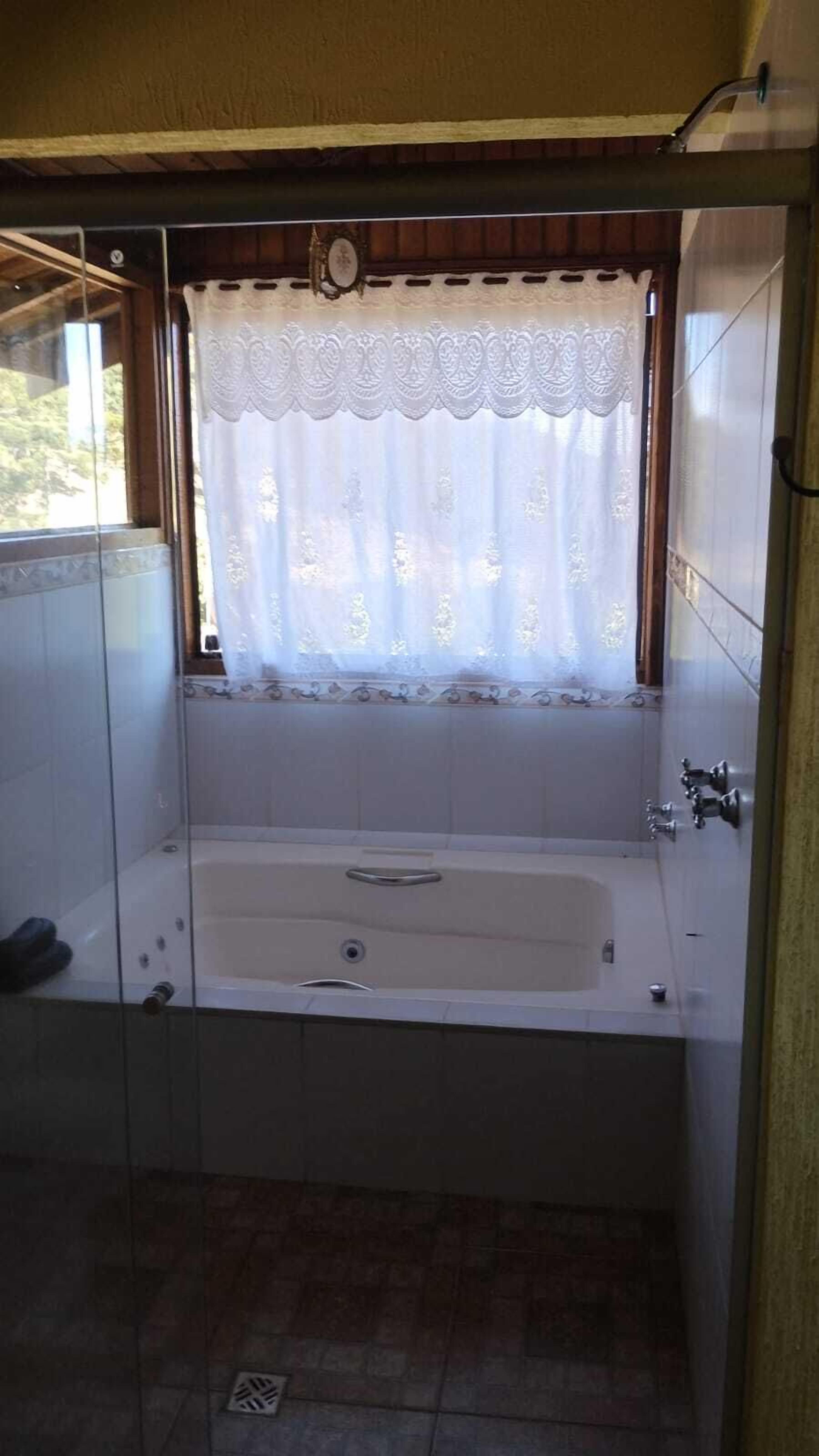 A bathroom with a bathtub, a window with a decorative curtain, and a shower area.