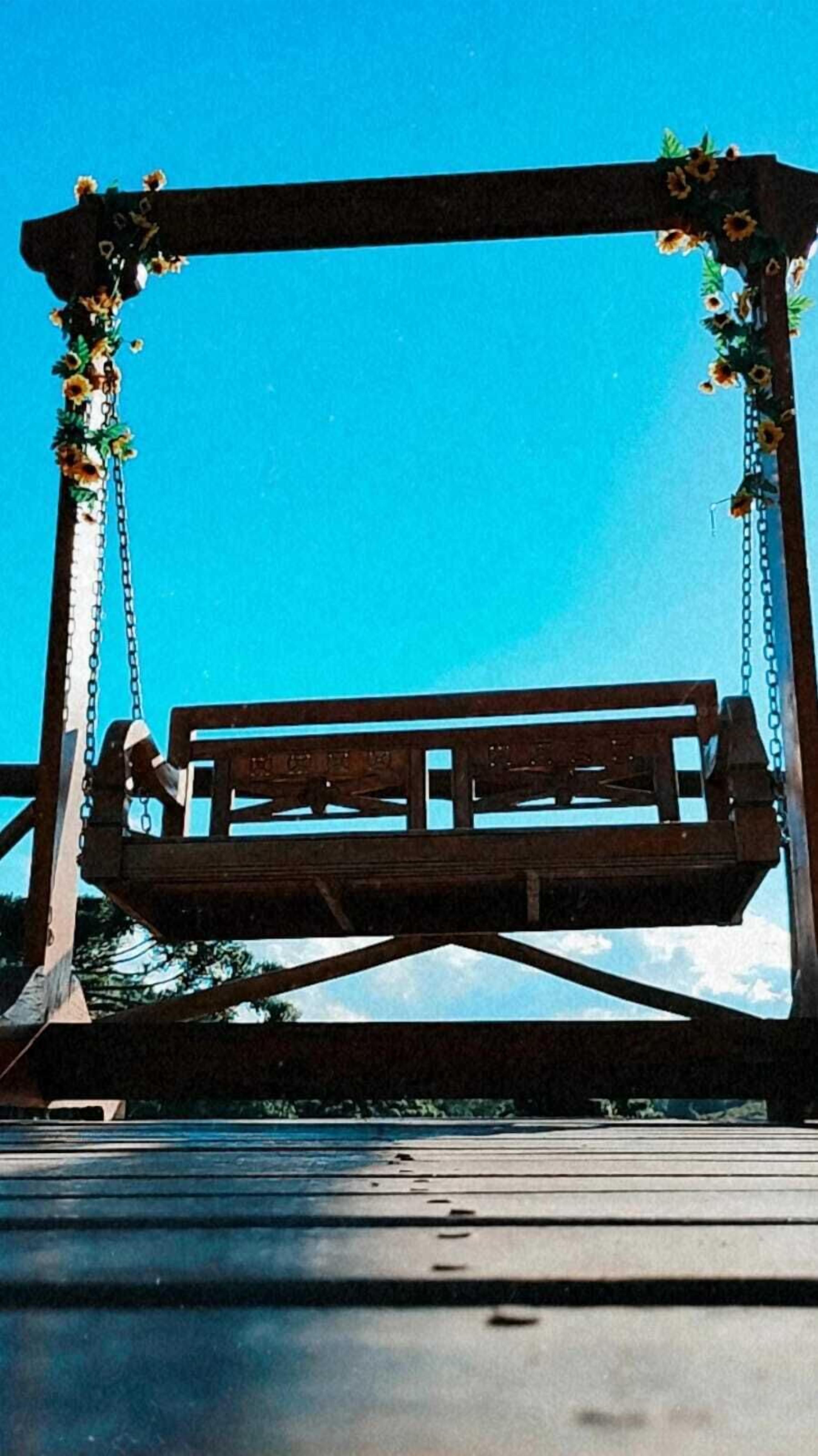 A wooden swing set with a bench, surrounded by a metal frame and decorated with flowers.
