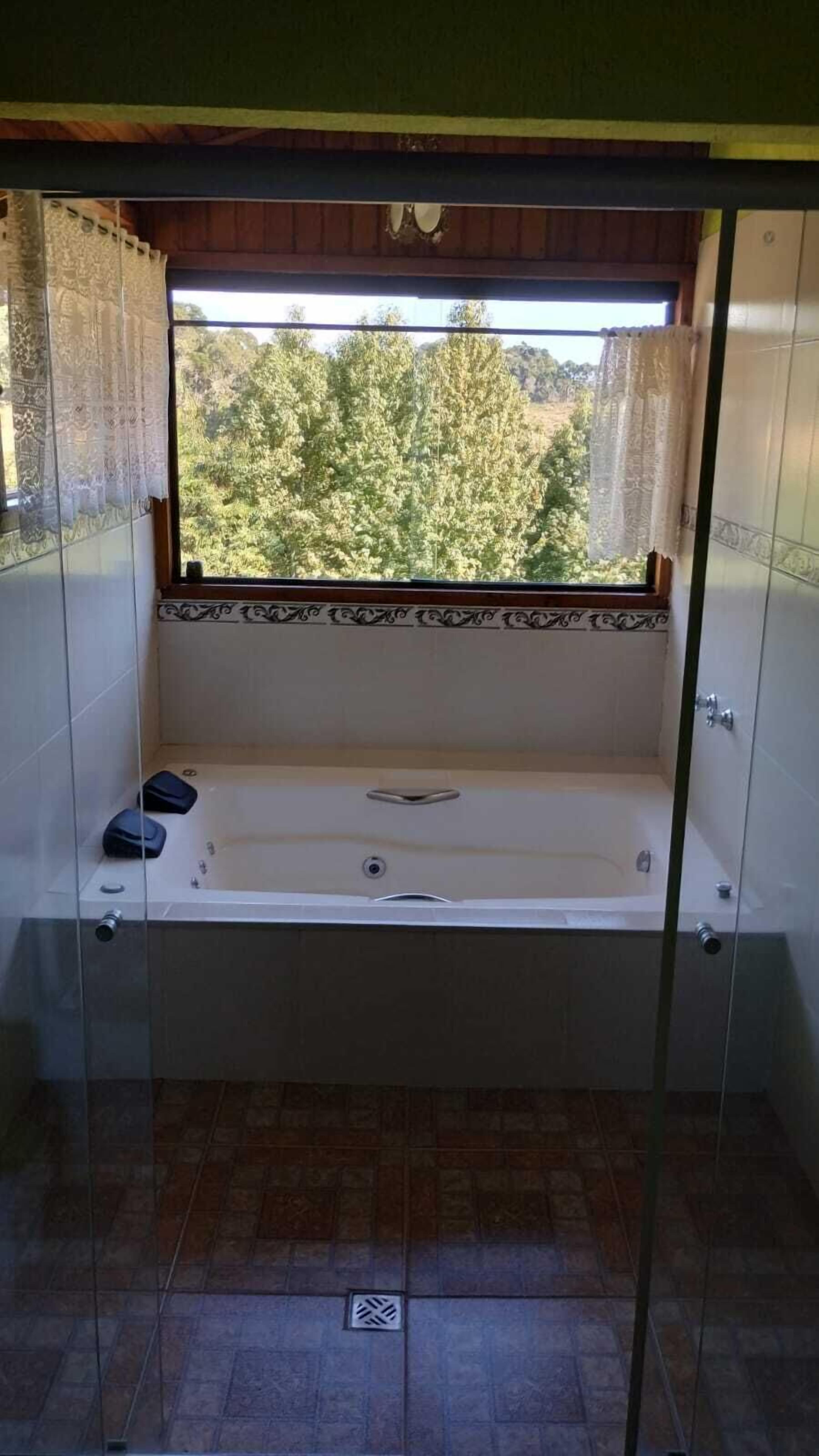 A small, enclosed bathroom with a bathtub, a window, and a view of trees outside.
