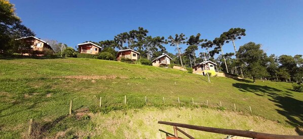 A hillside with several small cabins, surrounded by trees and a clear sky. - Canto dos Pássaros (Santo Antonio do Pinhal)