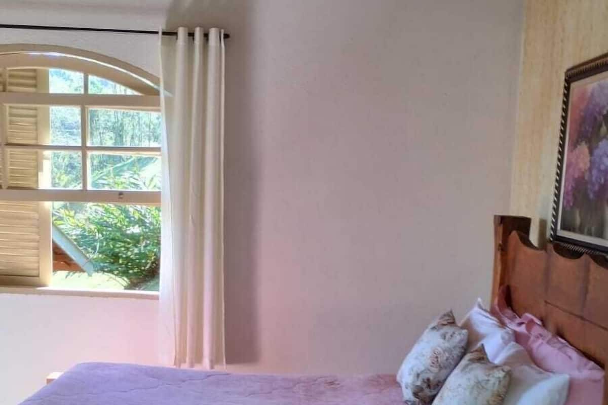 Ein Schlafzimmer mit einem Bett, einem Fenster mit Vorhängen, einer Holzbalkendecke und einem Bild an der Wand.