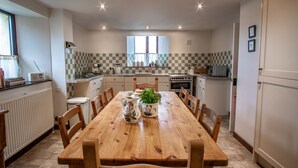 A kitchen with a wooden dining table, chairs, a window, and a checkered backsplash. - Wheelhouse (Barnstaple)