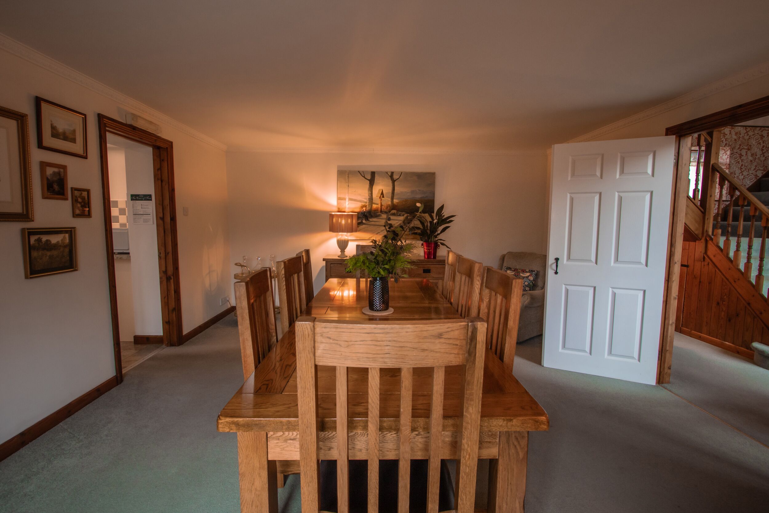 A dining area with a wooden table and chairs, a vase with a plant, and a painting on the wall.