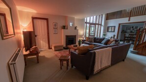 A cozy living room with a fireplace, a sofa, a coffee table, and a dining area in the background. - Wheelhouse (Barnstaple)