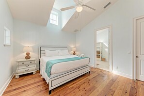 A bedroom with a bed, nightstands, a ceiling fan, and a view of a staircase.