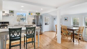 A modern kitchen with white cabinetry, stainless steel appliances, and a wooden dining table with chairs. - Beachgrass Bungalow by Seaside Vacations & Sales (Chincoteague Island)