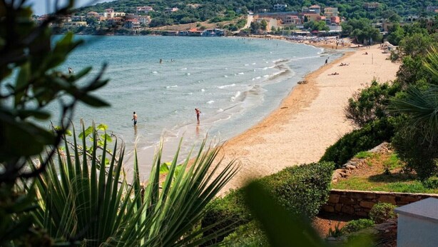 A beach with clear water, a sandy shore, and buildings in the background. - Sideratos Apartments (Karfas)