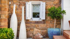 A stone wall with a window, two white vases, a fish sculpture, and a potted plant. - Sideratos Apartments (Karfas)