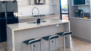 A modern kitchen with a central island, bar stools, pendant lighting, and built-in appliances. - HOP Encanto Exclusiva de Campo en Pisco (El Carmen)