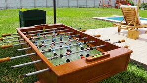 A foosball table in an outdoor setting with a pool table and lounge chairs nearby. - HOP Encanto Exclusiva de Campo en Pisco (El Carmen)