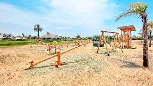 A playground with seesaws and swings, surrounded by palm trees and a building in the background. - HOP Canc n Hermosa Casa de Playa (El Carmen)