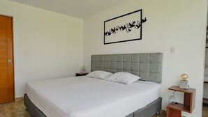 A modern bedroom with a large bed, a grey headboard, a bedside table with a lamp, and a wall art piece. - HOP Praia Exclusiva Laguna y Playa en Chincha (El Carmen)