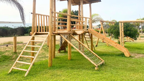 A wooden playground structure with a covered play area, slides, and climbing features. - HOP Praia Exclusiva Laguna y Playa en Chincha (El Carmen)