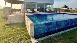 A modern house with a swimming pool, glass doors, and a covered patio with lounge chairs. - HOP Aruba Exclusiva Oasis y Playa en Chincha (El Carmen)