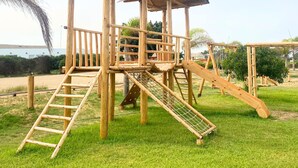 A wooden playground structure with a covered play area, slides, and climbing features. - HOP Bali Exclusiva Laguna y Playa en Chincha (El Carmen)