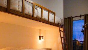 A bunk bed with a wooden frame and white bedding, a small bedside table with a light, and a view of the outside through a window with curtains. - HOP Macao Hermosa Casa de Playa (El Carmen)