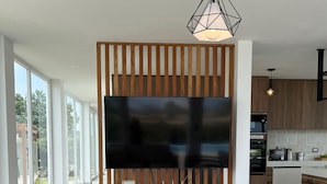 Ein modernes Wohnzimmer mit großem Flachbildfernseher, Holzvertäfelung, weißen Möbeln und einem Esstisch mit Topfpflanze.
