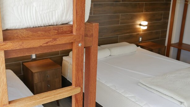 Ein Stockbett mit Holzleiter, ein Nachttisch mit Lampe und eine Matratze.