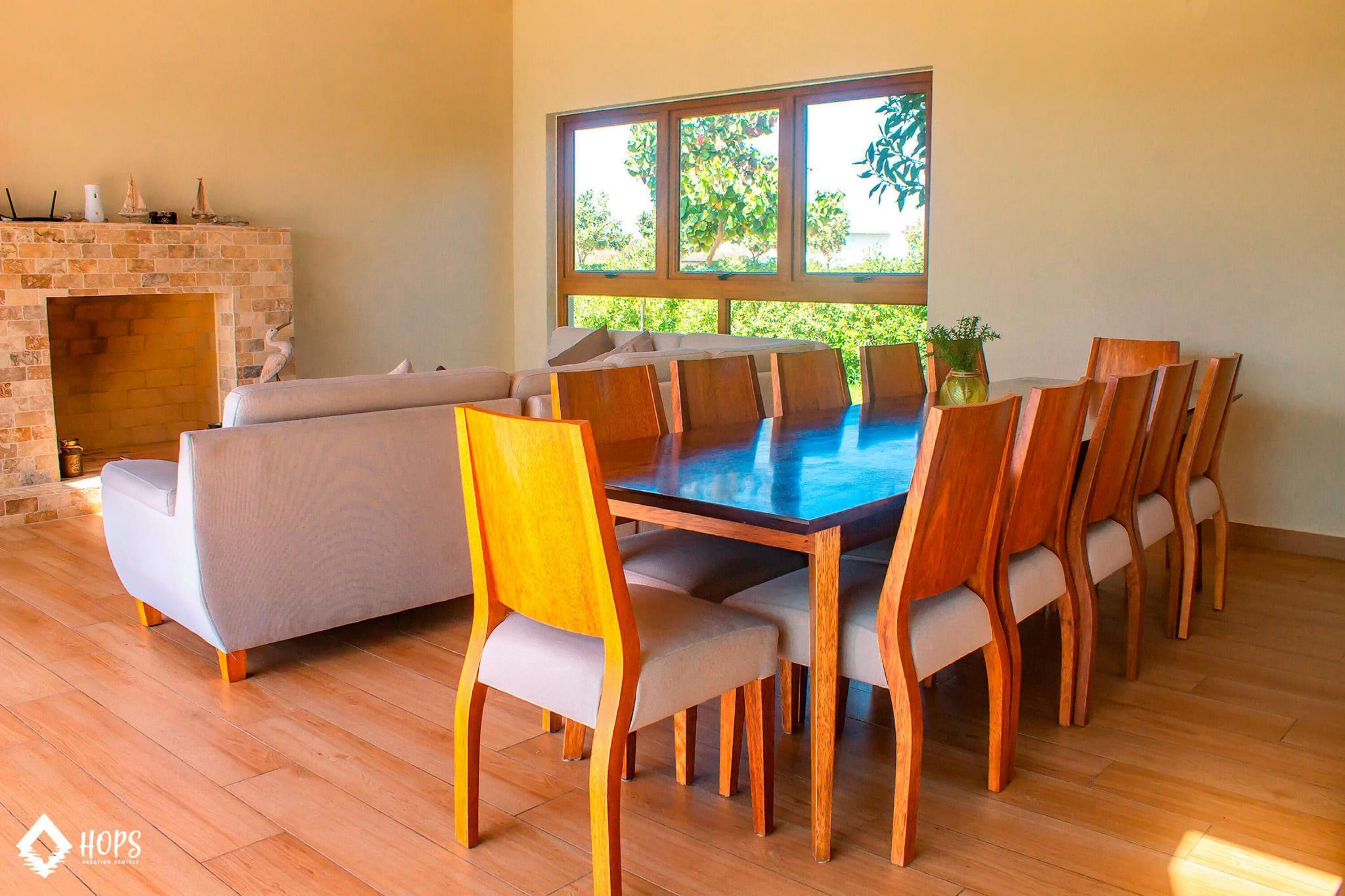 A dining area with a wooden table and chairs, a fireplace, and a large window with a view of greenery.