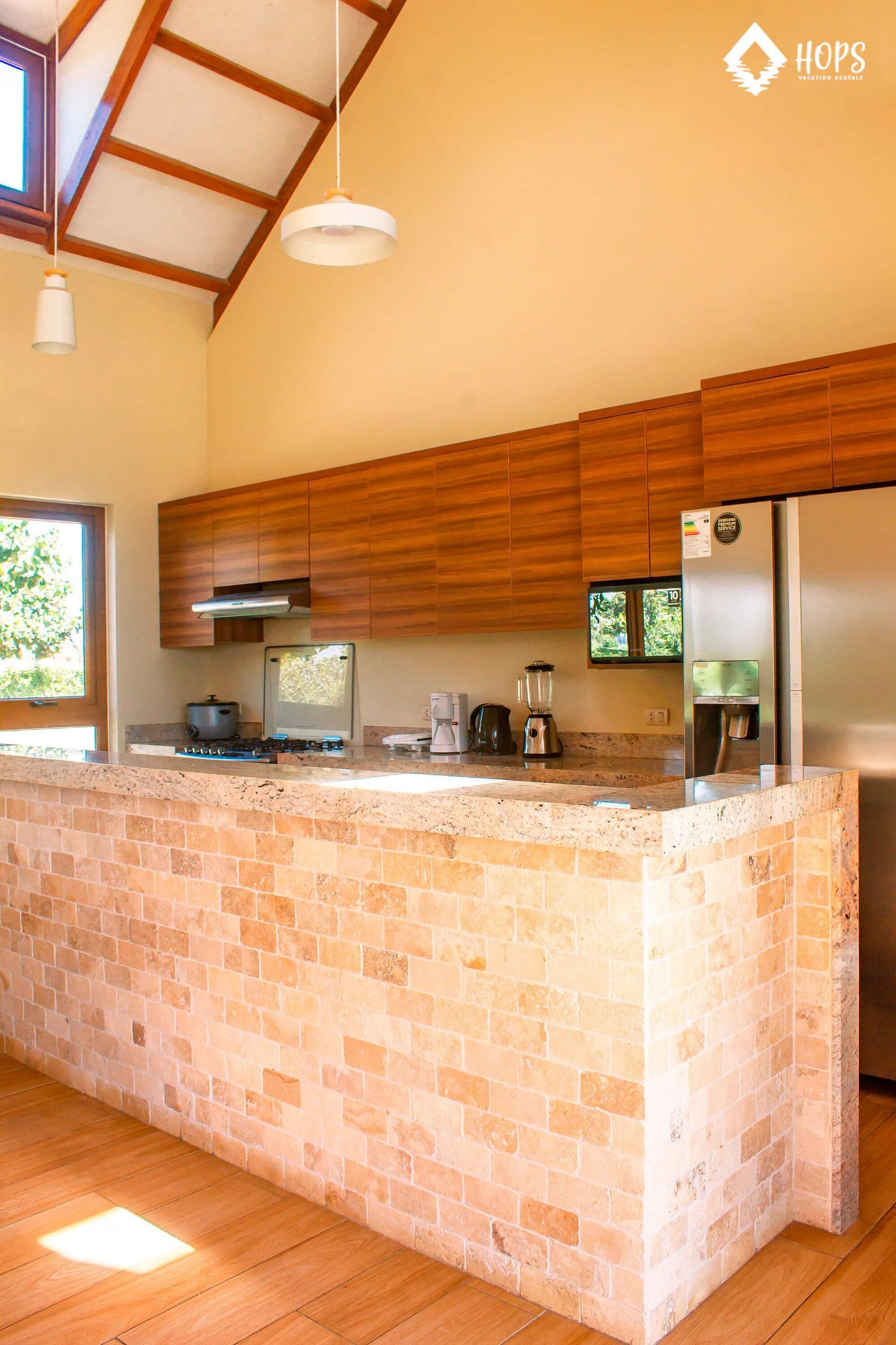 A kitchen with a brick island, wooden cabinets, stainless steel appliances, and pendant lighting.
