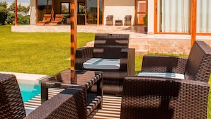 A covered outdoor seating area with wicker furniture and a pool in the background. - HOP Lago MAR Exclusiva en Playa de Chincha (Sunampe)
