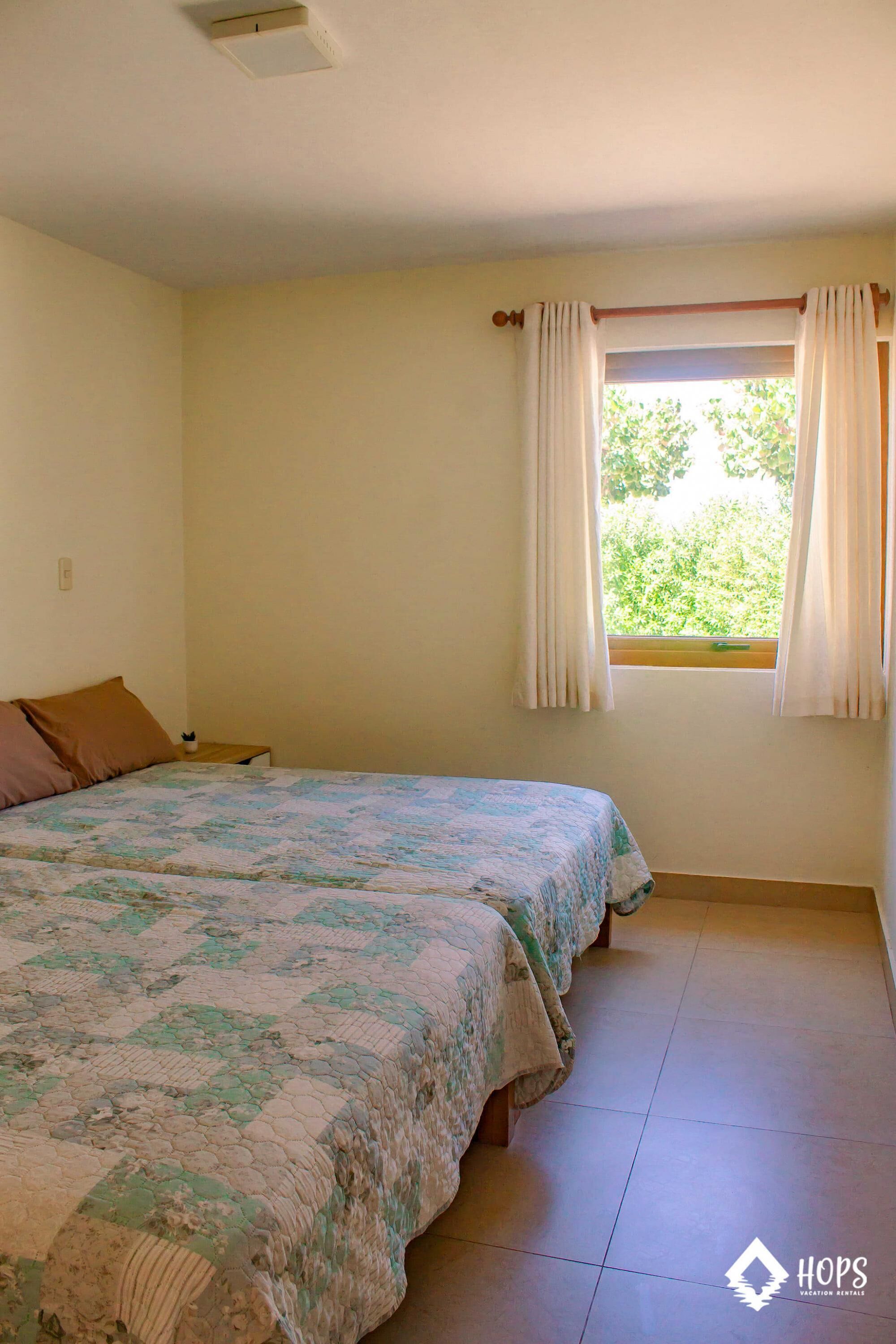Ein Zimmer mit zwei Betten, einem Vorhangfenster und einem Fliesenboden.