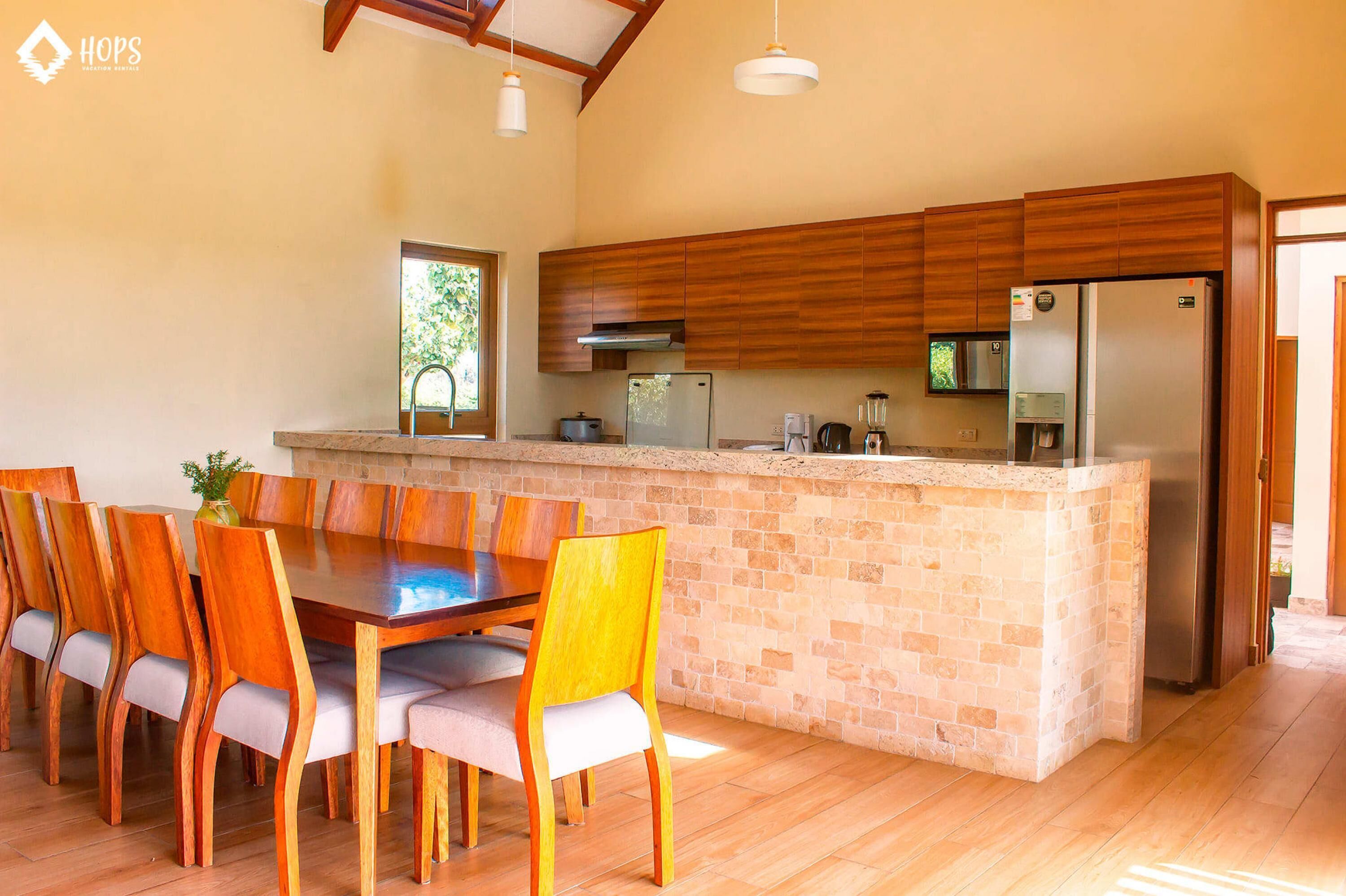 A modern kitchen with a central island, wooden cabinets, and a dining area with chairs.